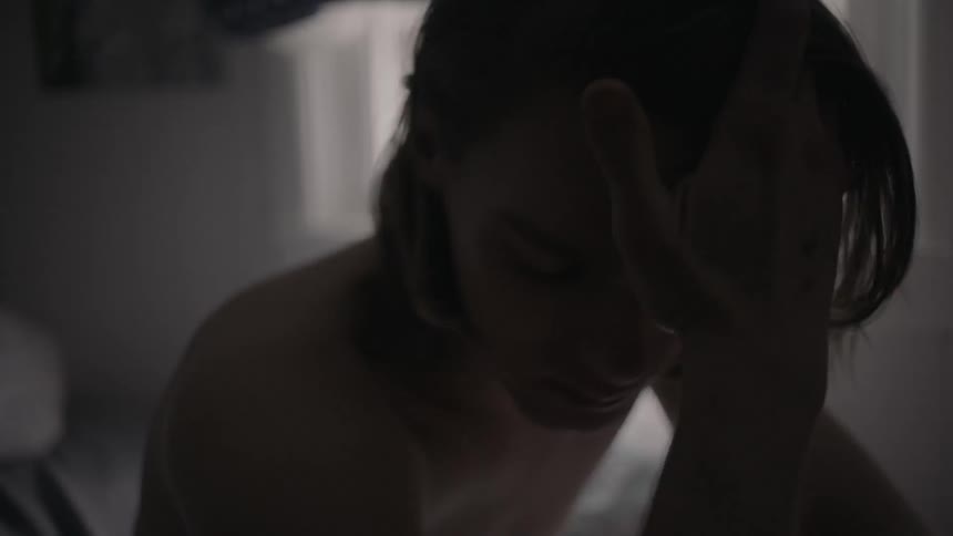 Shirtless long-haired man pondering something in a dimly lit room
