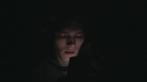 A man is looking at an electronic device in the dark