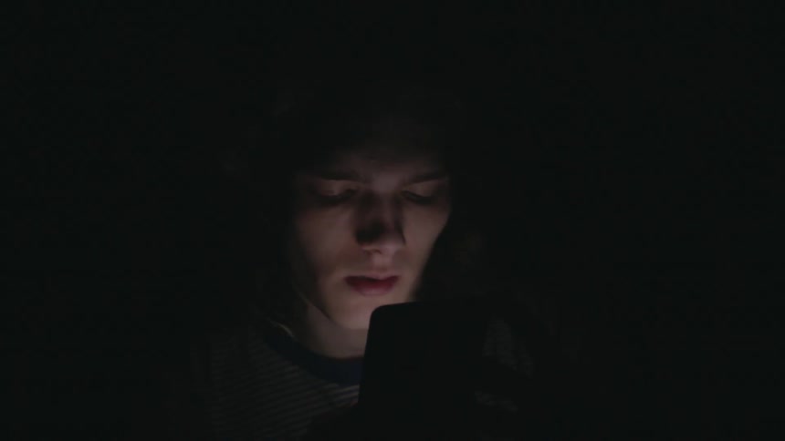 A man is looking at an electronic device in the dark