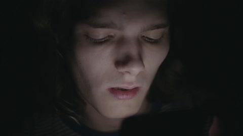 A man is looking at a screen giving off light in a pitch black area