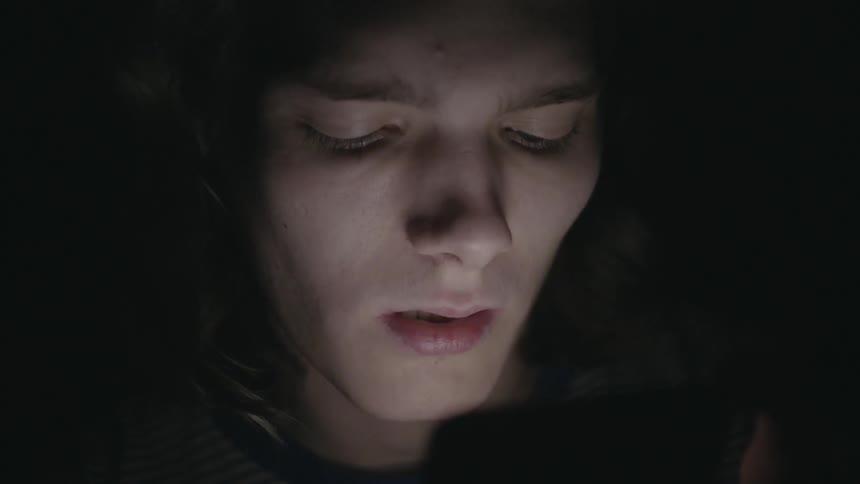 A man is looking at a screen giving off light in a pitch black area
