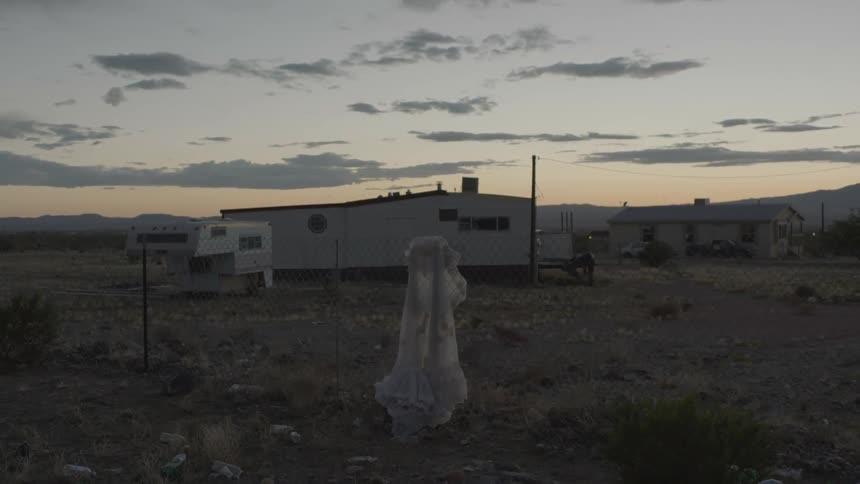 An old white dress hung on a fence blows in the breeze near two homes