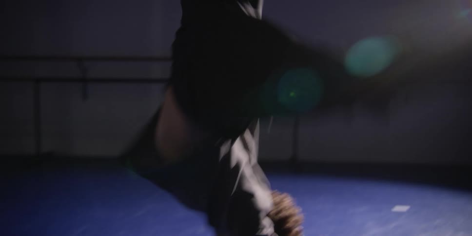 A man dancing in a dark stage lit only by a spotlight behind him