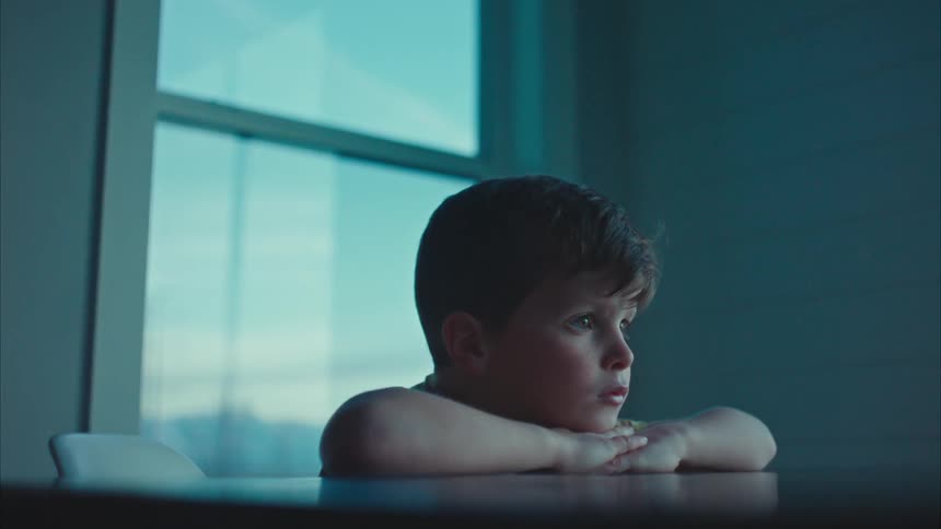 A boy thinking as he rests his chin on his hands crossed on a table