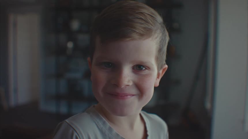 A little boy looking intently forward is smiling with his mouth closed and blinking his eyes
