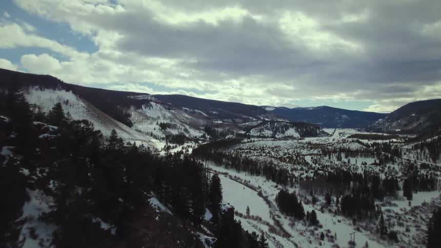 An aerial view of a region with several hills full of pine trees and lots of snow on the ground