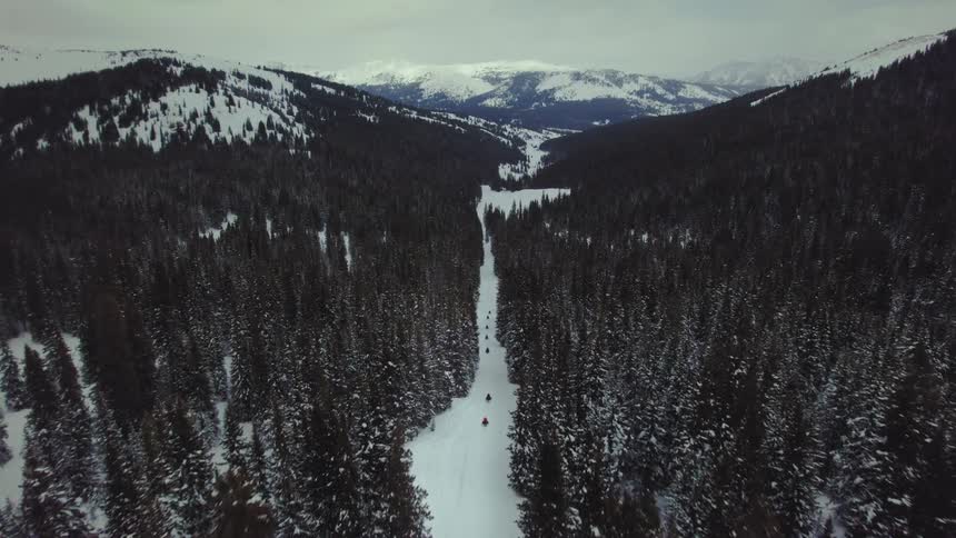 Aerial landscape of a path with people walking through the mountain covered in snow and with conifers around