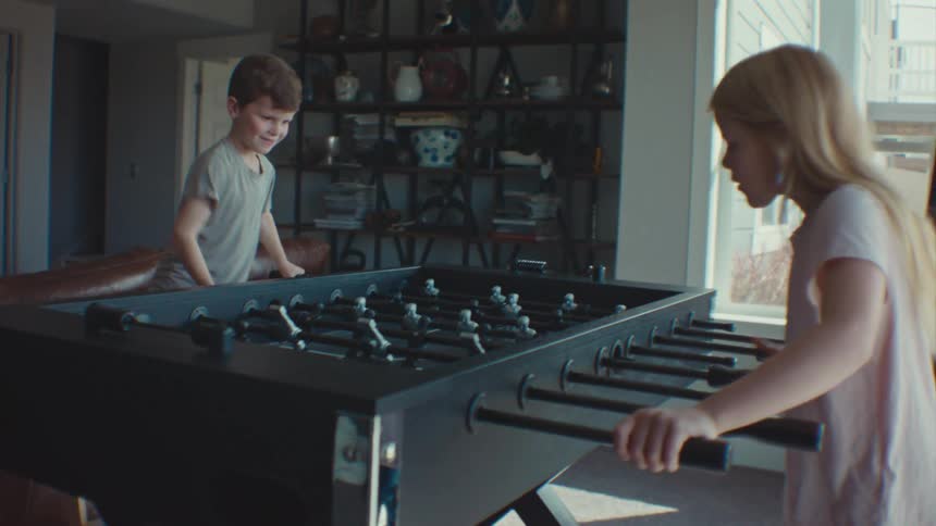 Male and female children playing table soccer inside the living room during the day