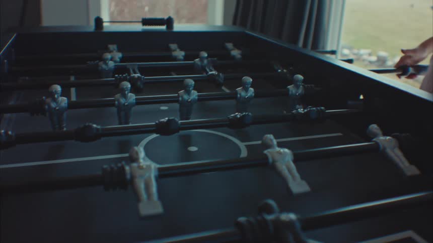A little blonde girl is playing foosball and is smiling