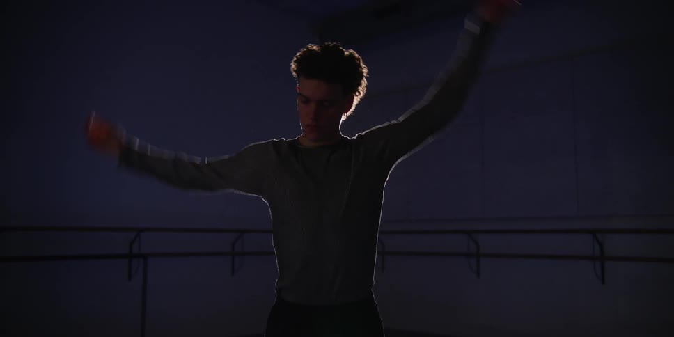 Man dancer inside a room with low lighting stretching his arms