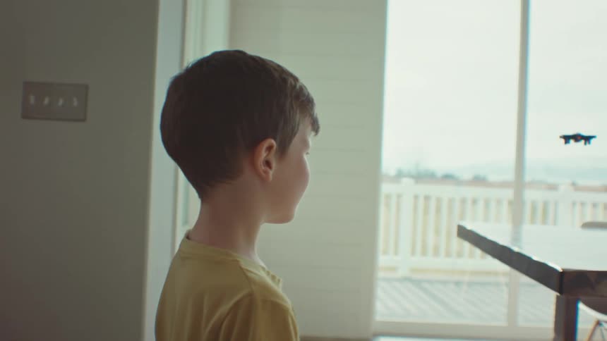 Little boy holding a remote control and playing with a small plane that flies around the room