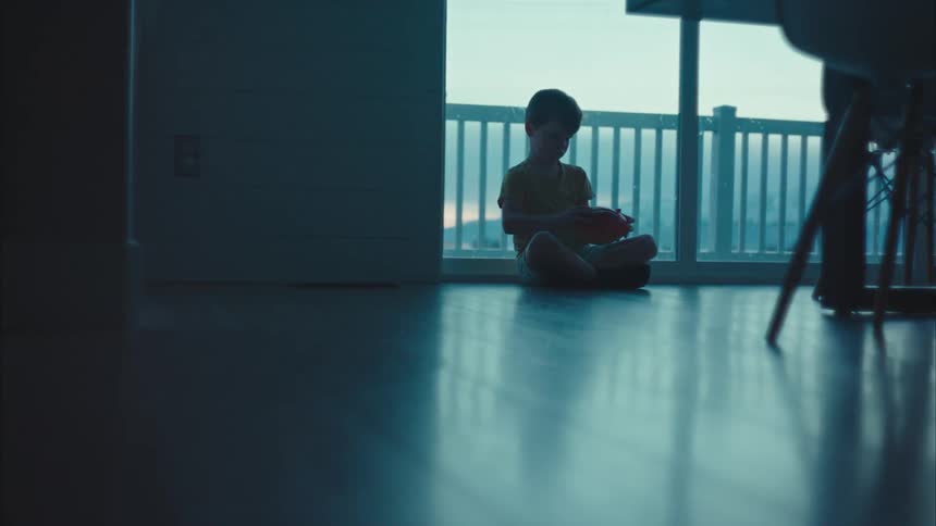 A little boy sits on the floor of a room with a balcony behind it