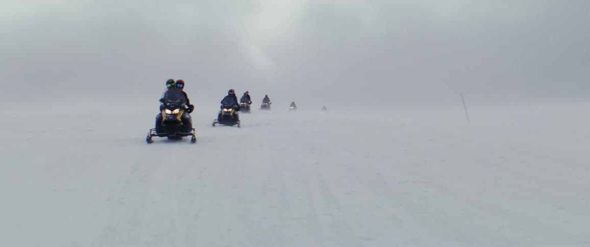 Group of people riding snowmobiles down a snowcovered mountain on a cloudy day