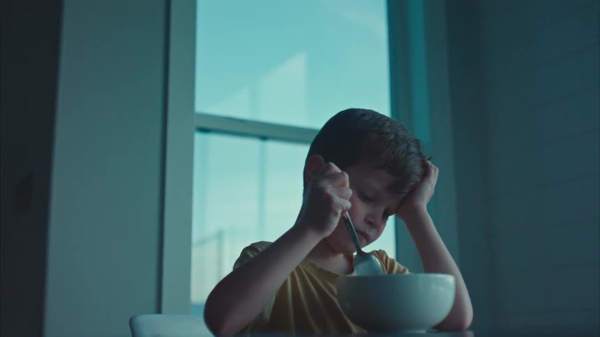 A sad boy eating cereal alone at the dining table