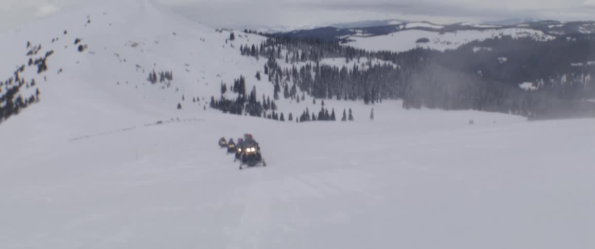 Several people ride snowmobiles near a mountain