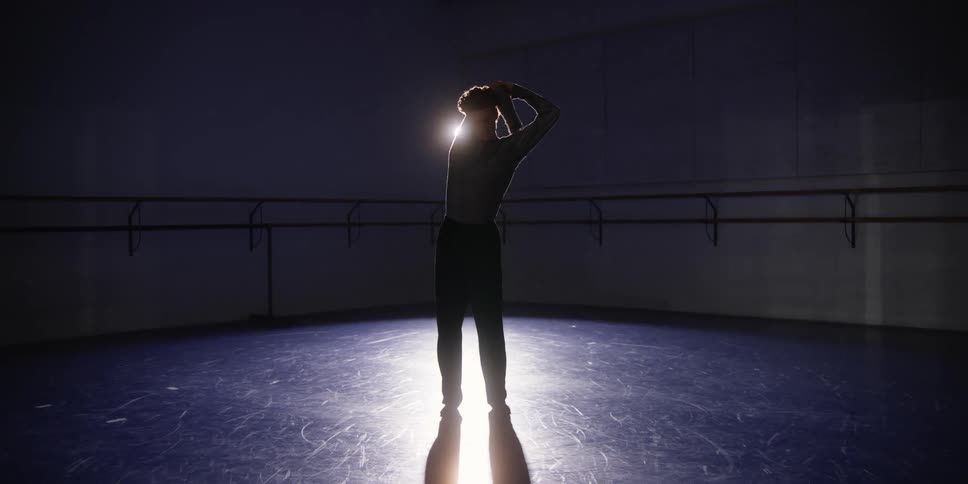 Dancer in a room with low lighting stretching his arms