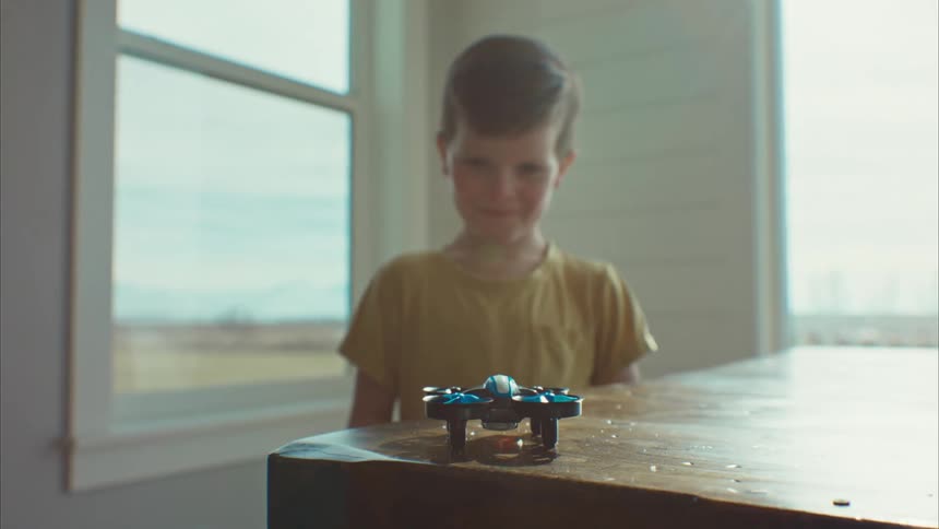 A young boy smiles excitedly as a small drone takes off from the table in front of him