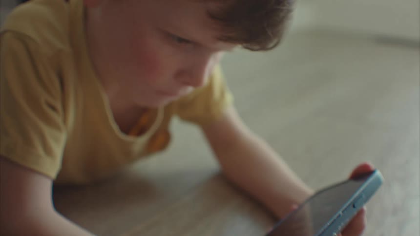 A young boy on the floor playing with a smart phone
