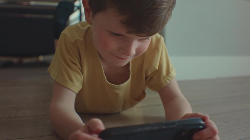 Little boy lying on the floor and concentrating while watching on cell phone