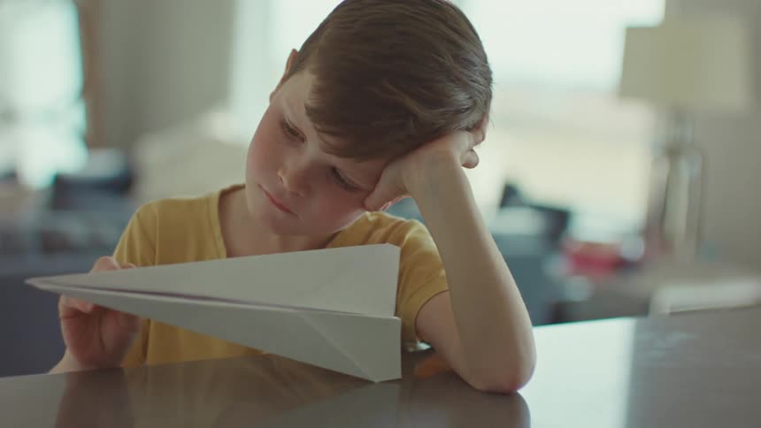 A young boy stares at a paper airplane