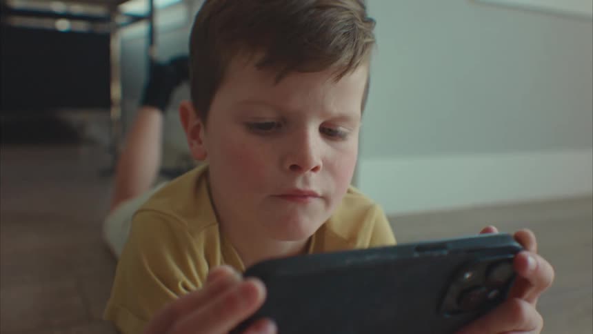 A young boy lying on the floor and playing with a smart phone