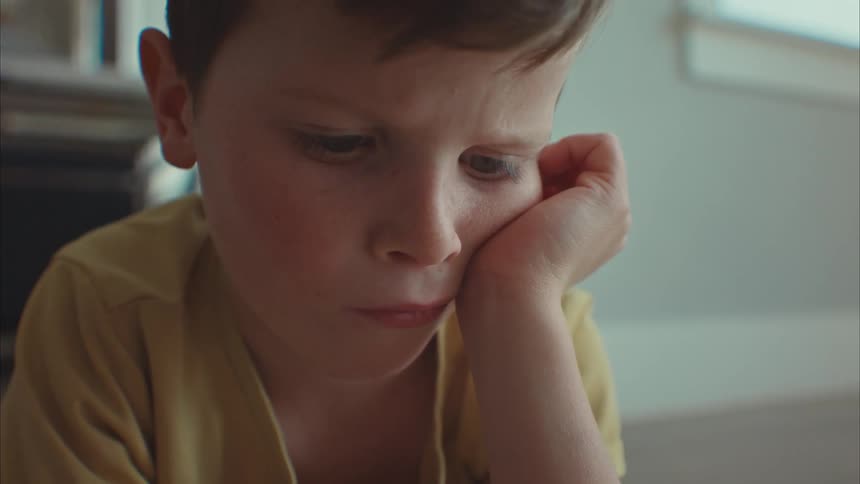 A boy lying on the floor his hand holding his face looking focused as he plays with a smart phone