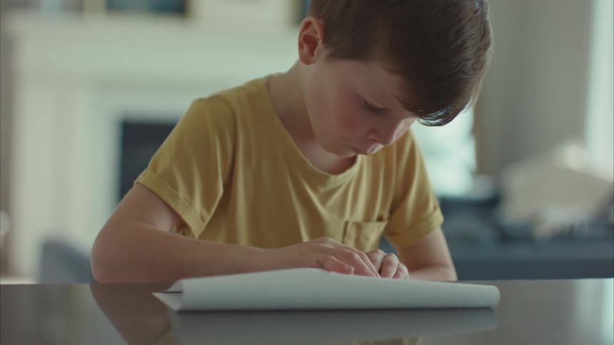 Little boy sitting at the table making a paper airplane