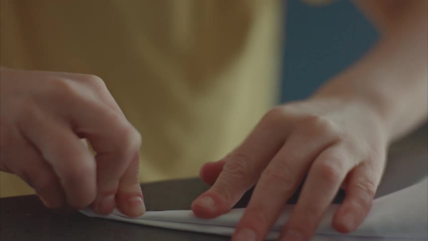 A young boy is making a paper airplane indoors