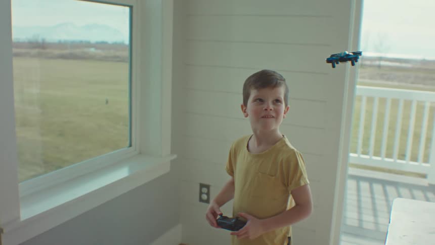 Little boy indoors using a remote control and controlling a small drone that flies