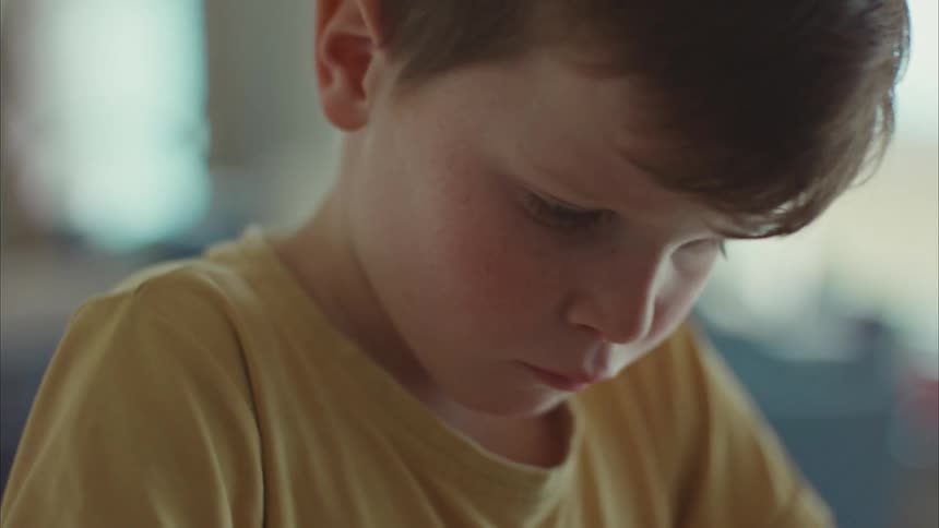 A young little boy in a yellow shirt is looking at a paper airplane he built