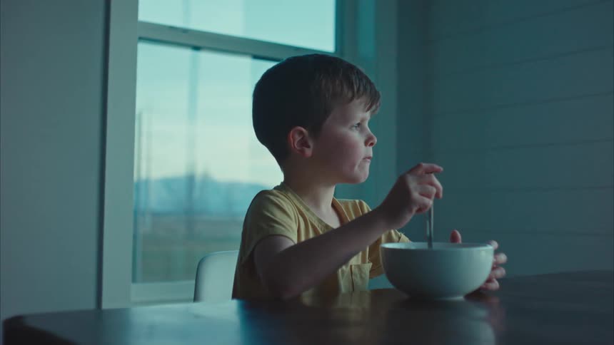 A boy eating a bowl of cereal sitting at the kitchen table