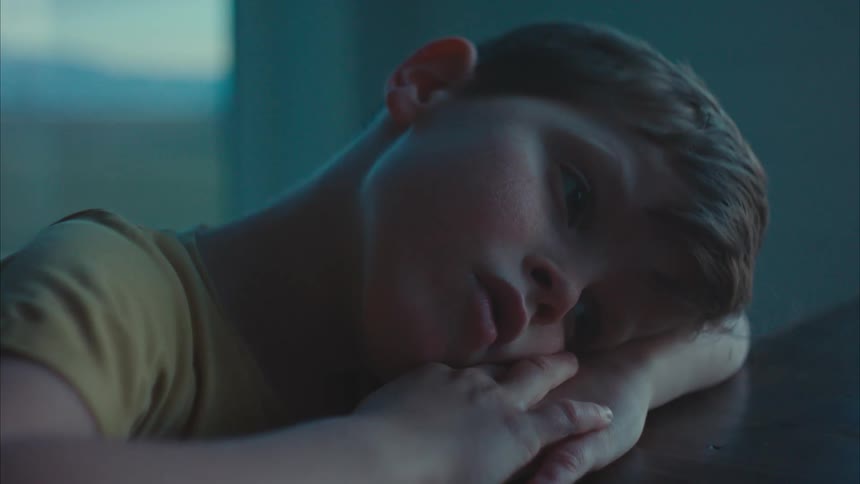 Portrait of a despondent little boy lying with his head on his arm on the table