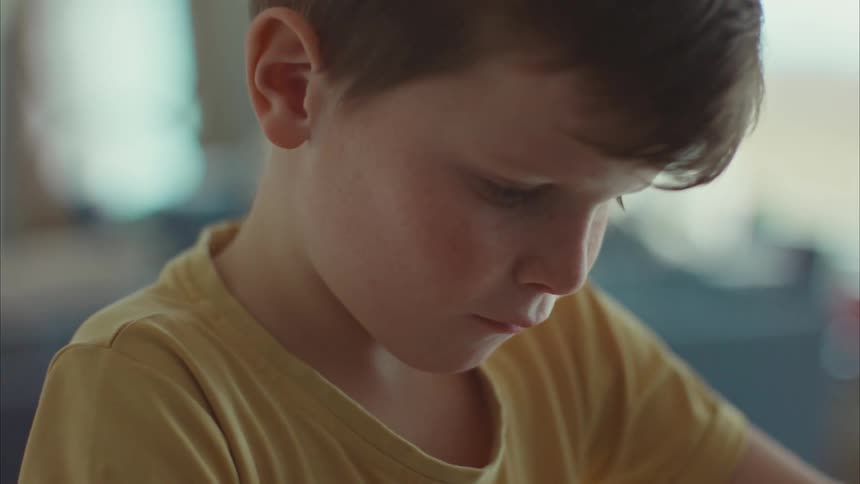 A young boy smiles and then concentrates as he folds a paper airplane