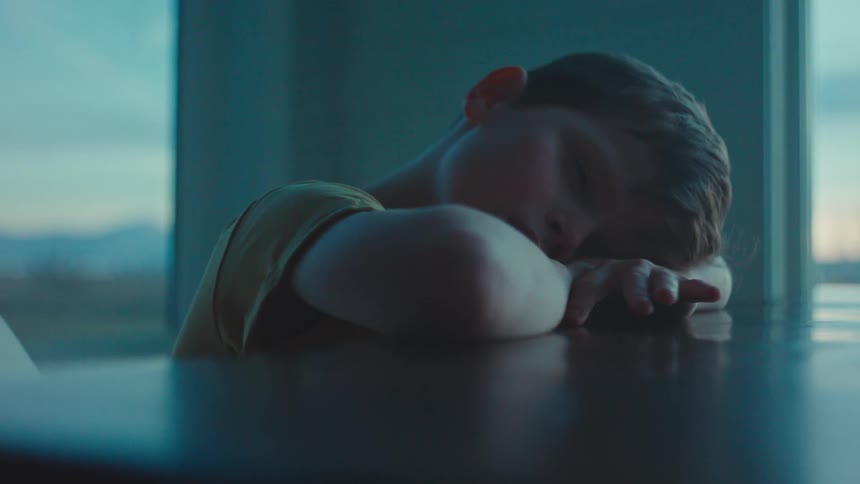 Portrait of a boy with his head and arms resting on the table looking sad