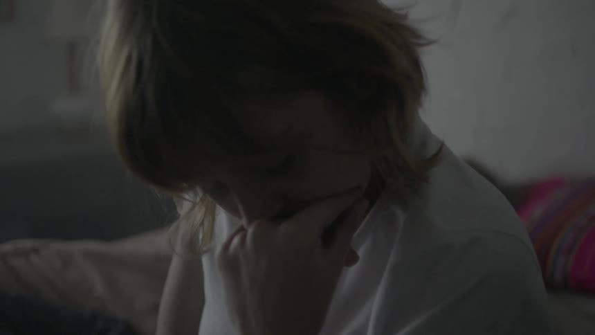 A woman sits and thinks on a bed