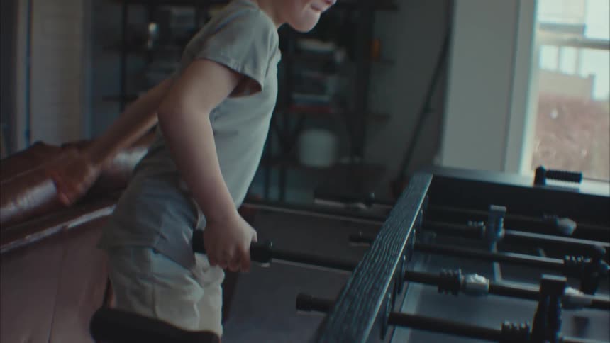 A boy child playing table soccer and smiling in the living room