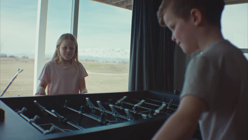 A little boy and a little girl are playing foosball and the little girl raises her arms up to celebrate
