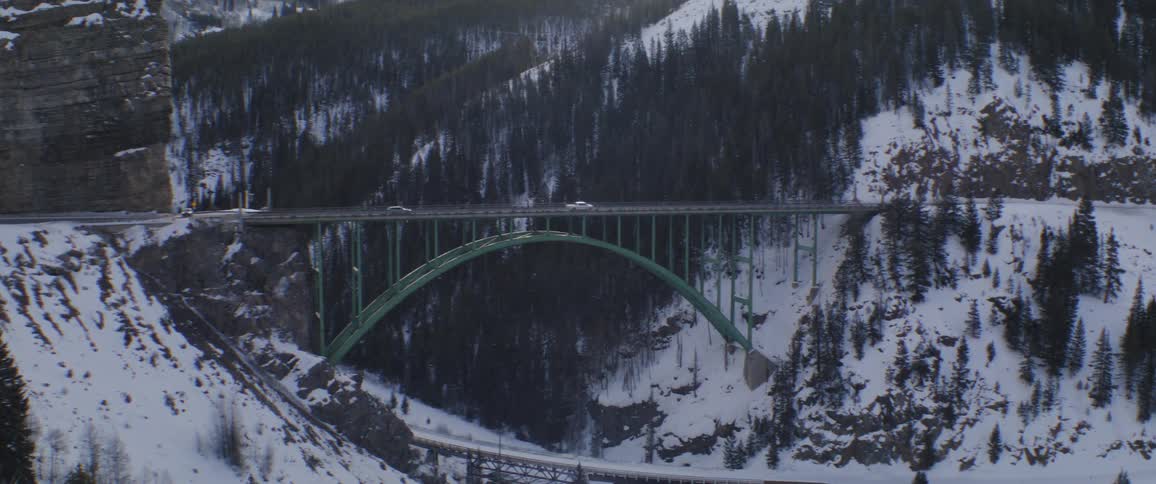 Several vehicles drive over a bridge in a mountain valley