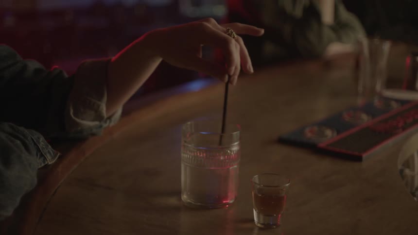 A person stirs their drink at a bar