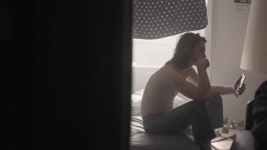A man sits on a bed looking at his phone