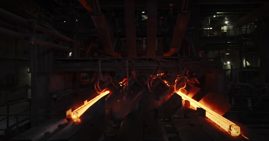Glowing metal beams push through large machines in a steel factory