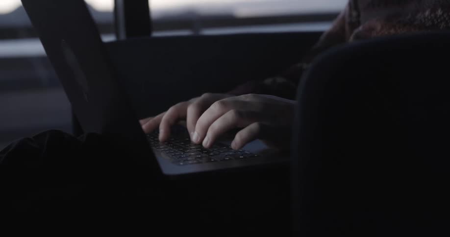 Man in a sweater sits in armchair working on laptop