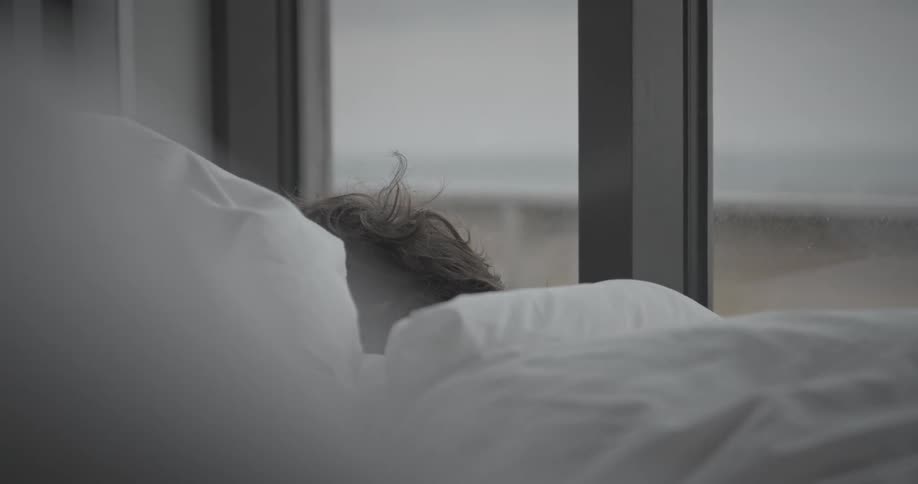 A person sleeps under a white blanket in bedroom