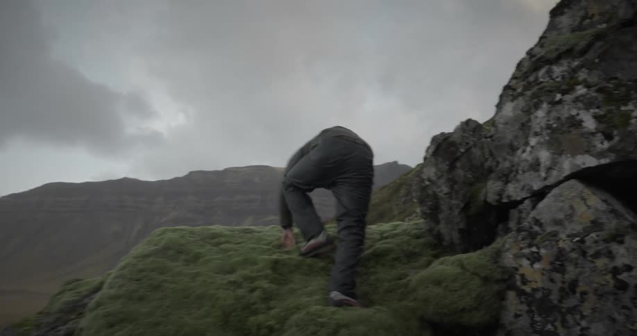 Man climbing rocks on a mountain with his back turned on a cloudy day