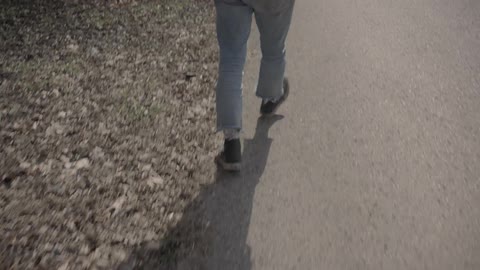 A man walks on a road with leaves scattered on the roadside