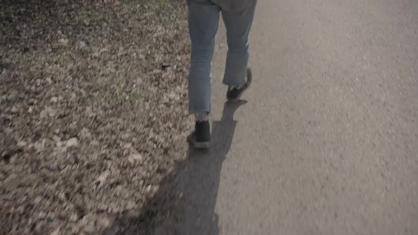 A man walks on a road with leaves scattered on the roadside