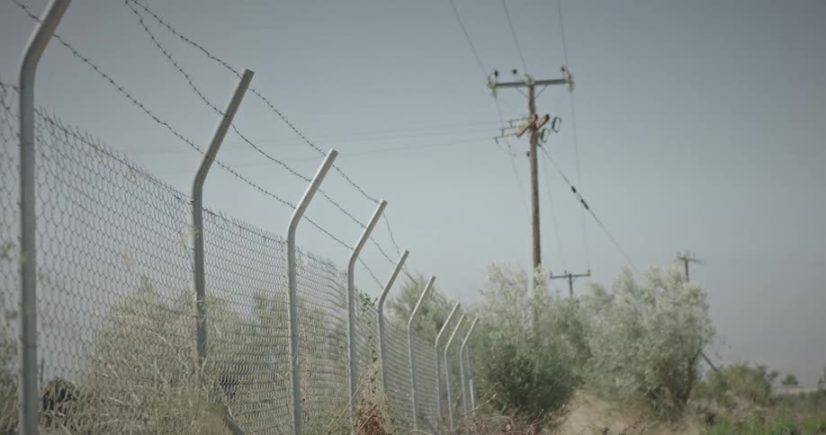 Utility pole towers over chain link fence enclosing field on a windy day