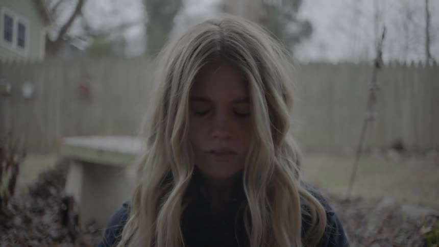 A young woman stands outdoors and opens her eyes