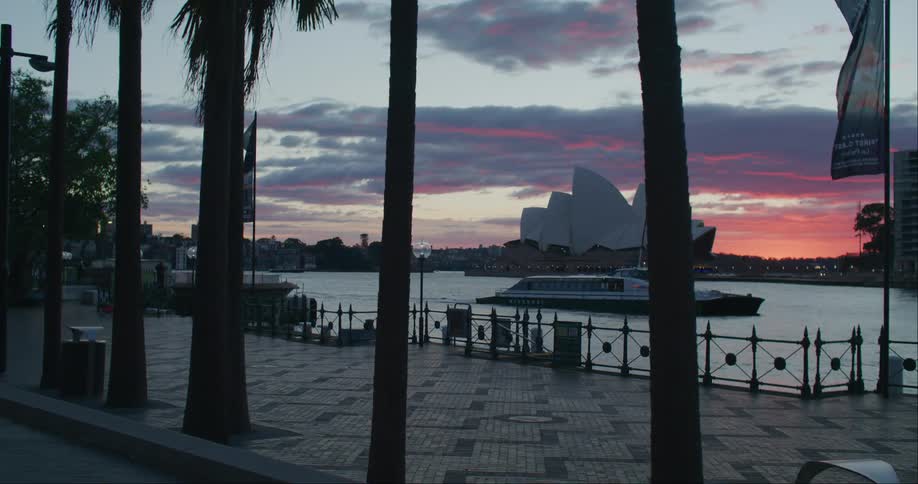 Tourist boat passing through the sea next to the city of sydney in a late afternoon with a red sky