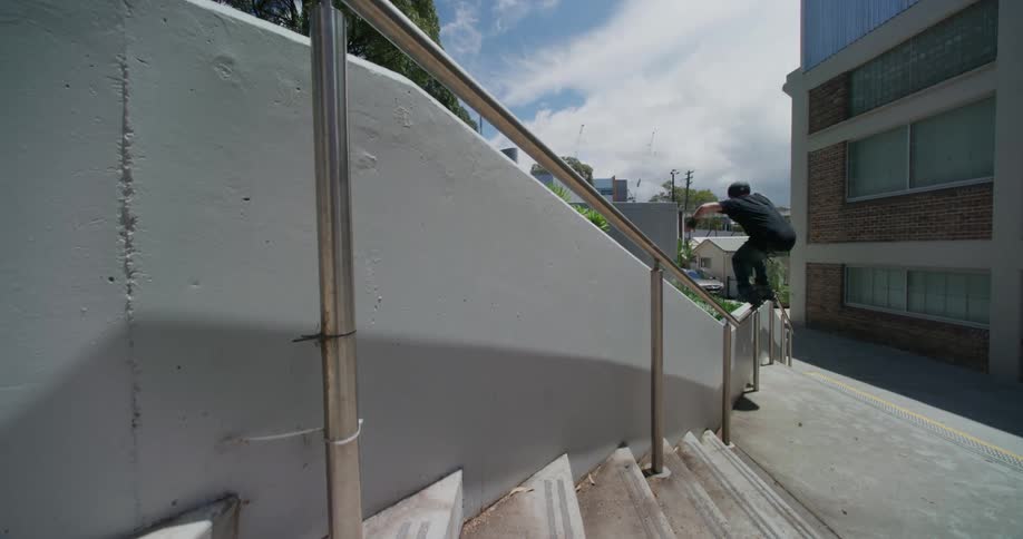 A man on roller skates grinds over a concrete wall on to a railing landing safely at the bottom